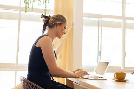 Young woman working at home from her living room couch with laptop on her lap. Home office concept. Gray notebook for working. Home office concept. high quality photoの写真素材
