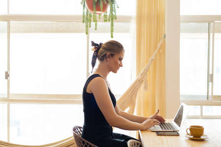 Young woman working at home in his kitchen with laptop and papers on kitchen wooden desk. Home office concept. Gray notebook for working. Home office concept. high quality photoの写真素材