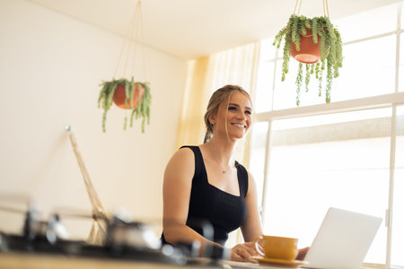 Young woman working at home in his kitchen with laptop and papers on kitchen wooden desk. Home office concept. Gray notebook for working. Home office concept. high quality photoの写真素材