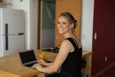 Young woman working at home in his kitchen with laptop and papers on kitchen wooden desk. Home office concept. Gray notebook for working. Home office concept. high quality photoの写真素材