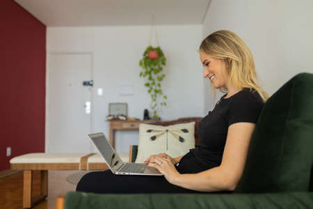 Young woman working at home in his kitchen with laptop and papers on kitchen wooden desk. Home...