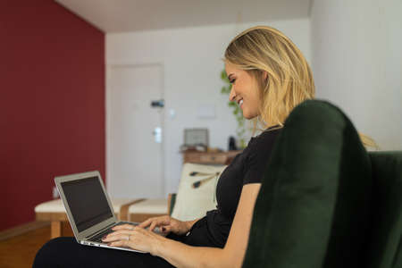 Young woman working at home in his kitchen with laptop and papers on kitchen wooden desk. Home office concept. Gray notebook for working. Home office concept. high quality photoの写真素材