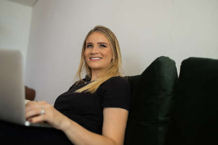 Young woman working at home from her living room couch with laptop on her lap. Home office concept. Gray notebook for working. Home office concept. high quality photoの写真素材