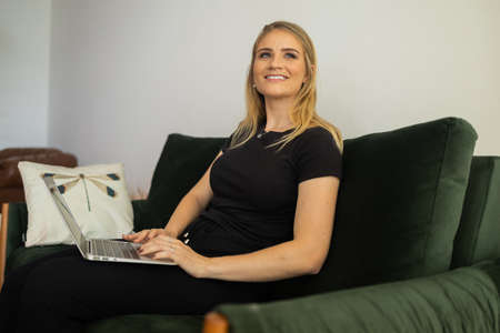 Young woman working at home from her living room couch with laptop on her lap. Home office concept. Gray notebook for working. Home office concept. high quality photoの写真素材