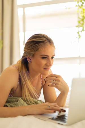 Young woman working at home from her living room couch with laptop on her lap. Home office concept. Gray notebook for working. Home office concept. high quality photoの写真素材