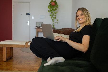Young woman working at home from her living room couch with laptop on her lap. Home office concept....