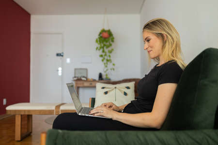 Young woman working at home from her living room couch with laptop on her lap. Home office concept. Gray notebook for working. Home office concept. high quality photoの写真素材