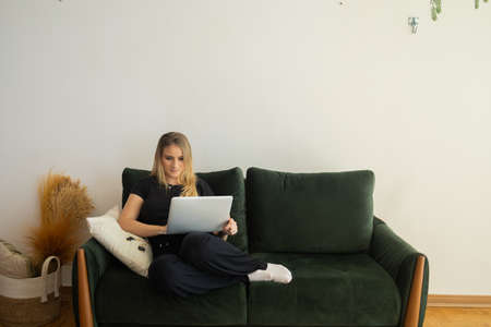 Young woman working at home from her living room couch with laptop on her lap. Home office concept. Gray notebook for working. Home office concept. high quality photoの写真素材