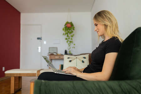 Young woman working at home from her bedroom with laptop on her bed. Woman lying down. Home office concept. Gray notebook for working. Cozy and comfortable. Home office concept. high quality photoの写真素材