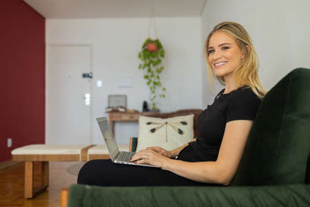 Young woman working at home from her bedroom with laptop on her bed. Woman lying down. Home office concept. Gray notebook for working. Cozy and comfortable. Home office concept. high quality photoの写真素材