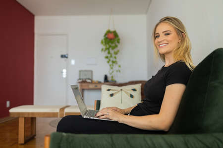 Young woman working at home from her bedroom with laptop on her bed. Woman lying down. Home office concept. Gray notebook for working. Cozy and comfortable. Home office concept. high quality photoの写真素材