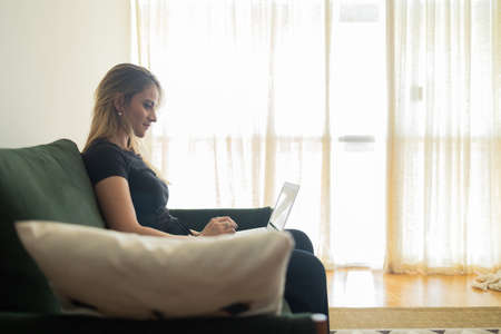 Young woman working at home from her bedroom with laptop on her bed. Woman lying down. Home office concept. Gray notebook for working. Cozy and comfortable. Home office concept. high quality photoの写真素材
