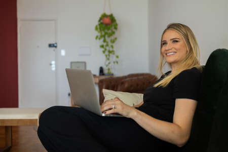 Young woman working at home from her bedroom with laptop on her bed. Woman lying down. Home office concept. Gray notebook for working. Cozy and comfortable. Home office concept. high quality photoの写真素材