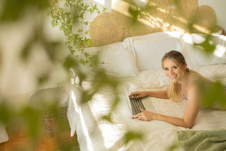Young woman working at home from her bedroom with laptop on her bed. Woman lying down. Home office concept. Gray notebook for working. Cozy and comfortable. Home office concept. high quality photoの写真素材