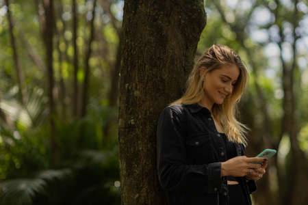 Young woman using a smartphone at day time with a green park in the background. High quality photo. Mobile phone, technology, urban concept. high quality photoの写真素材
