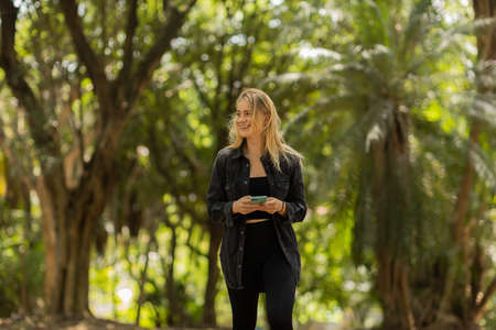 Young woman using a smartphone at day time with a green park in the background. High quality photo. Mobile phone, technology, urban concept. high quality photoの写真素材