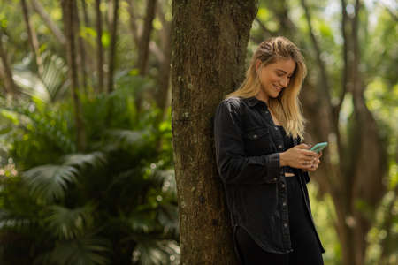 Young woman using a smartphone at day time with a green park in the background. High quality photo. Mobile phone, technology, urban concept. high quality photoの写真素材