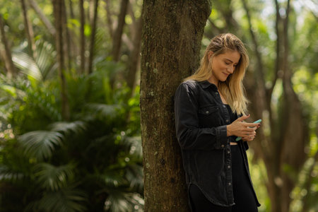 Young woman using a smartphone at day time with a green park in the background. High quality photo. Mobile phone, technology, urban concept. high quality photoの写真素材