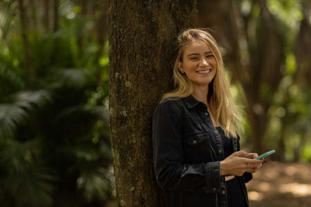 Young woman using a smartphone at day time with a green park in the background. High quality photo. Mobile phone, technology, urban concept. high quality photoの写真素材