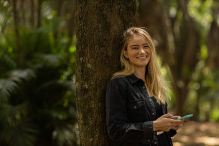 Young woman using a smartphone at day time with a green park in the background. High quality photo. Mobile phone, technology, urban concept. high quality photoの写真素材