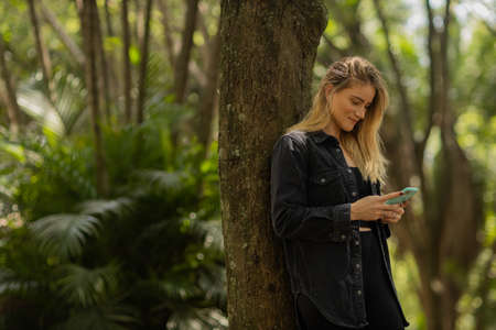 Young woman using a smartphone at day time with a green park in the background. High quality photo. Mobile phone, technology, urban concept. high quality photoの写真素材