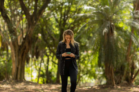 Young woman using a smartphone at day time with a green park in the background. High quality photo. Mobile phone, technology, urban concept. high quality photoの写真素材