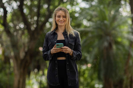 Young woman using a smartphone at day time with a green park in the background. High quality photo. Mobile phone, technology, urban concept. high quality photoの写真素材