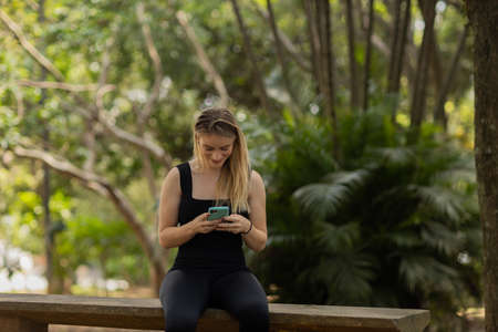 Young woman using a smartphone at day time with a green park in the background. High quality photo. Mobile phone, technology, urban concept. high quality photoの写真素材