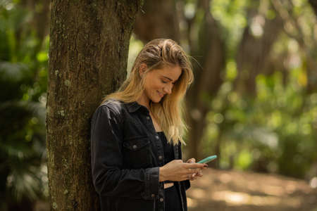 Young woman using a smartphone at day time with a green park in the background. High quality photo. Mobile phone, technology, urban concept. high quality photoの写真素材