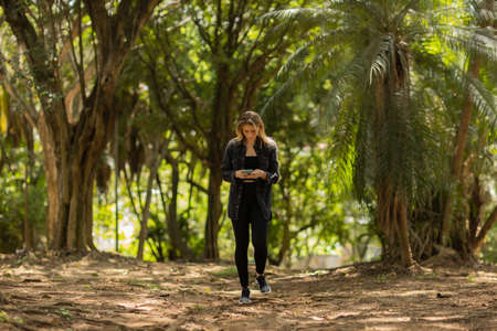 Young woman using a smartphone at day time with a green park in the background. High quality photo. Mobile phone, technology, urban concept. high quality photoの写真素材