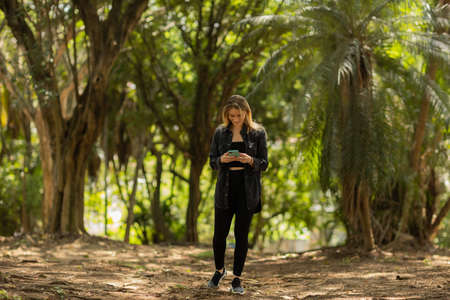 Young woman using a smartphone at day time with a green park in the background. High quality photo. Mobile phone, technology, urban concept. high quality photoの写真素材