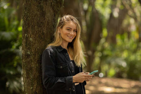 Young woman using a smartphone at day time with a green park in the background. High quality photo. Mobile phone, technology, urban concept. high quality photoの写真素材