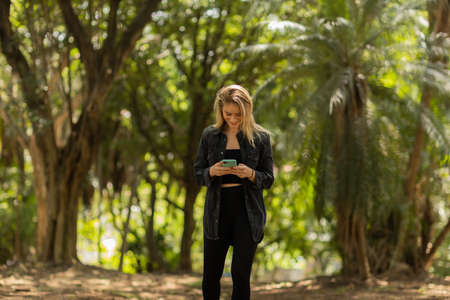 Young woman using a smartphone at day time with a green park in the background. High quality photo. Mobile phone, technology, urban concept. high quality photoの写真素材