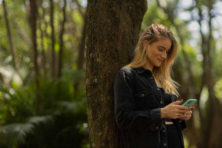 Young woman using a smartphone at day time with a green park in the background. High quality photo. Mobile phone, technology, urban concept. high quality photoの写真素材
