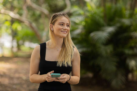 Young woman using a smartphone at day time with a green park in the background. High quality photo. Mobile phone, technology, urban concept. high quality photoの写真素材