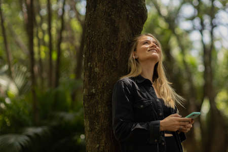 Young woman using a smartphone at day time with a green park in the background. High quality photo. Mobile phone, technology, urban concept. high quality photoの写真素材