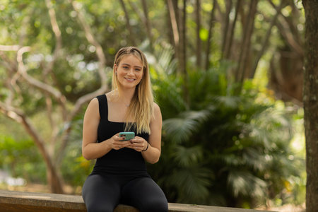 Young woman using a smartphone at day time with a green park in the background. High quality photo. Mobile phone, technology, urban concept. high quality photoの写真素材