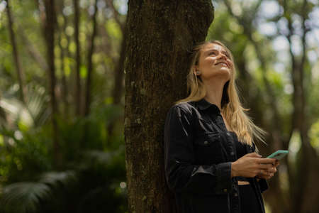 Young woman using a smartphone at day time with a green park in the background. High quality photo. Mobile phone, technology, urban concept. high quality photoの写真素材