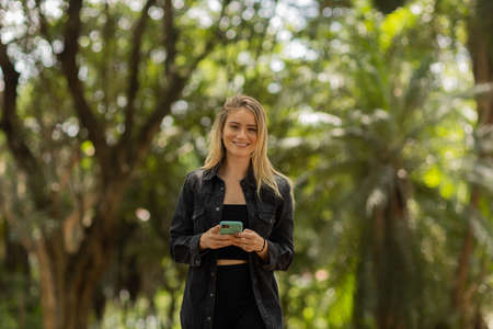 Young woman using a smartphone at day time with a green park in the background. High quality photo. Mobile phone, technology, urban concept. high quality photoの写真素材