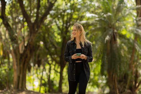 Young woman using a smartphone at day time with a green park in the background. High quality photo. Mobile phone, technology, urban concept. high quality photoの写真素材
