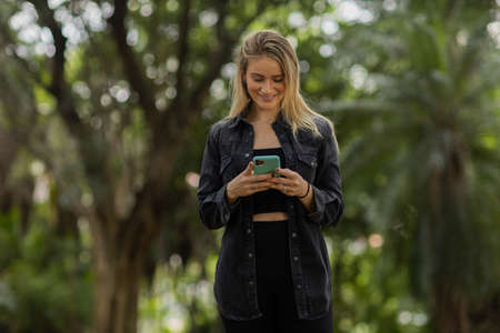 Young woman using a smartphone at night time with city view landscape in the background. High quality photo. photo. Mobile phone, technology, urban concept.の写真素材