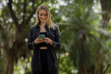 Young woman using a smartphone at night time with city view landscape in the background. High quality photo. photo. Mobile phone, technology, urban concept.の写真素材