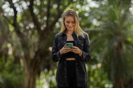 Young woman using a smartphone at night time with city view landscape in the background. High quality photo. photo. Mobile phone, technology, urban concept.の写真素材