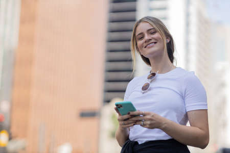 Young woman using a smartphone at night time with city view landscape in the background. High quality photo. photo. Mobile phone, technology, urban concept.の写真素材
