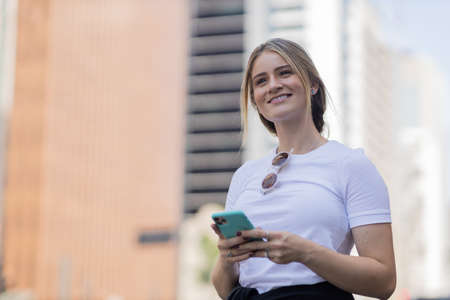 Young woman using a smartphone at night time with city view landscape in the background. High quality photo. photo. Mobile phone, technology, urban concept.の写真素材
