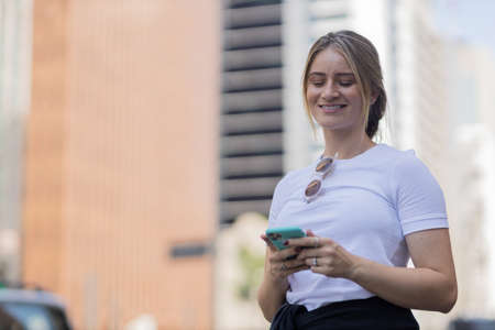 Young woman using a smartphone at night time with city view landscape in the background. High quality photo. photo. Mobile phone, technology, urban concept.の写真素材
