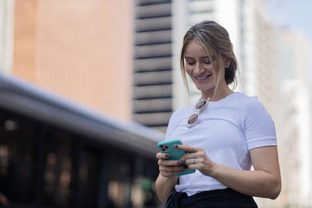 Young woman using a smartphone at night time with city view landscape in the background. High quality photo. photo. Mobile phone, technology, urban concept.の写真素材