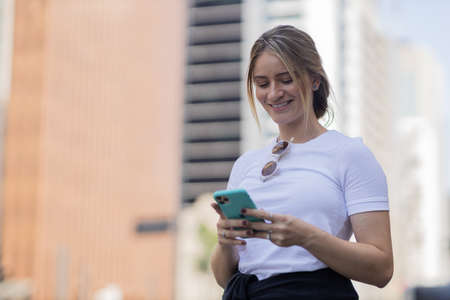 Young woman using a smartphone at night time with city view landscape in the background. High quality photo. photo. Mobile phone, technology, urban concept.の写真素材