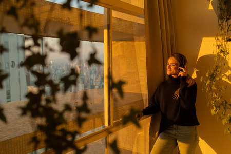 Young woman lying down on her apartment floor using a smartphone at night time with city view landscape in the background. High quality photo. Mobile phone, technology, concept. high quality photoの写真素材