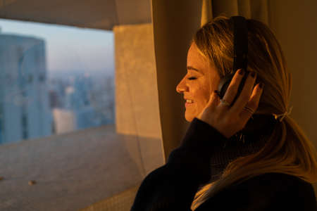 Young woman lying down on her apartment floor using a smartphone at night time with city view...